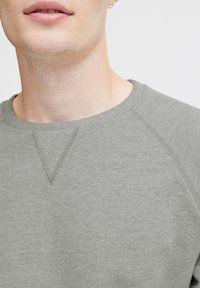 Sudadera gris claro con un cuello redondo acanalado y mangas raglán. La tela tiene una textura suave con un sutil patrón jaspeado.