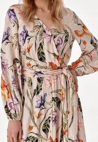 Blomsterindpakket kjole i lys beige med lilla, orange og pink blomster. Har lange ærmer, et bånd i taljen og knapdetaljer.