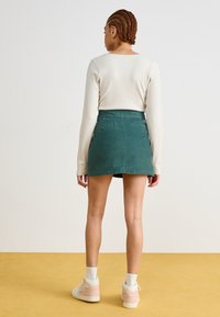 Πράσινη φούστα mini απ�ό κοτλέ με ευθεία άκρη, δύο πίσω τσέπες και κλείσιμο με κουμπί, συνδυασμένη με λευκό μακρυμάνικο μπλουζάκι με ριπ και ψηλές αθλητικές εσπαντρίγιες.