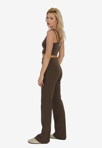 Brązowy prążkowany crop top z cienkimi ramiączkami w zestawie z pasującymi spodniami o wysokim stanie i szerokich nogawkach. Strój charakteryzuje się dopasowaną sylwetką i teksturowanym materiałem.