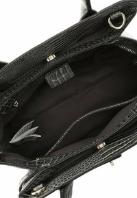 Intérieur de sac à main noir texturé crocodile montrant plusieurs compartiments, une poche zippée, une doublure en tissu et une étiquette d'entretien pliée.