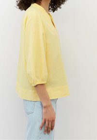 Żółta bawełniana bluzka z dekoltem w serek, rękawami o długości 3/4 z bufkami i luźnym krojem. Miękka tekstura, dół na wysokości bioder i delikatne marszczenie przy mankietach.