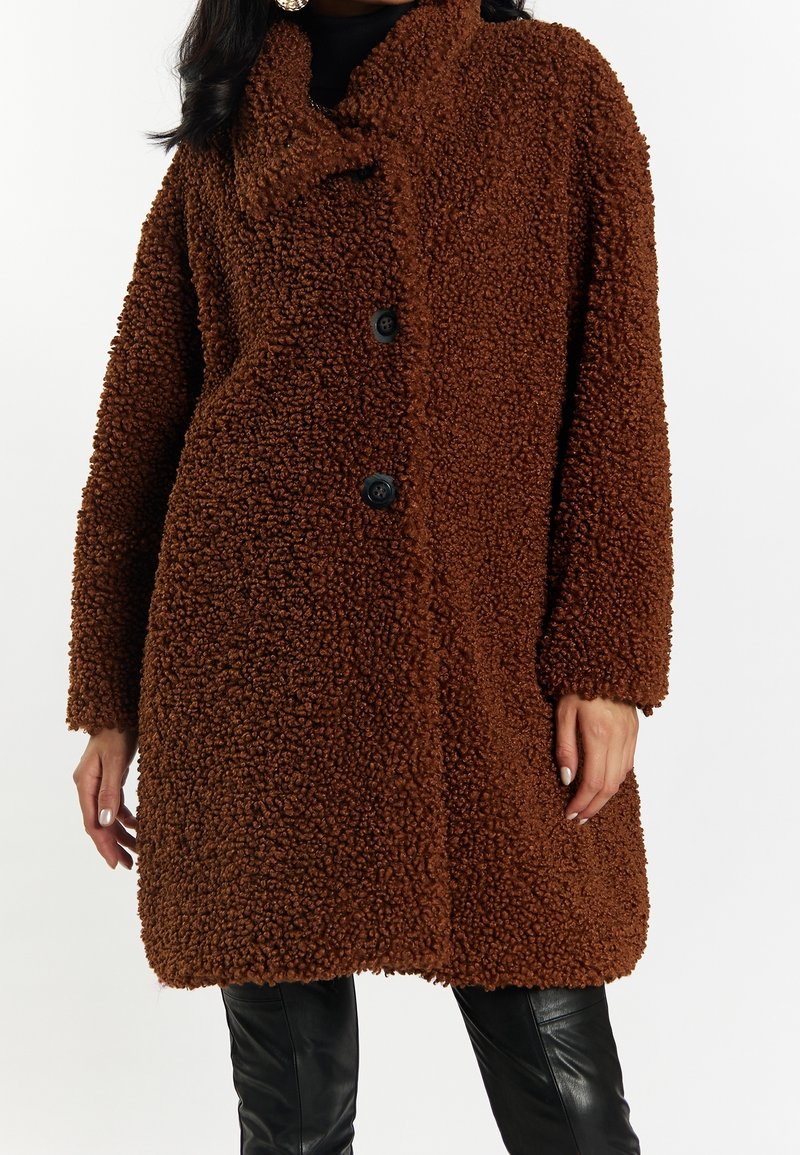 Brun, shaggy tekstureret frakke med frontknaplukning, stor krave og løs pasform. Sorte knapper kontrasterer med det bløde materiale.
