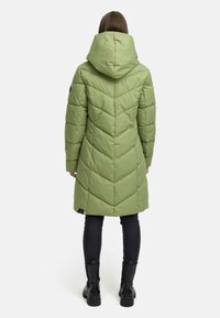 Long, hooded coat in soft green, featuring a quilted design with chevron patterns. Black pants and ankle boots complete the outfit.
