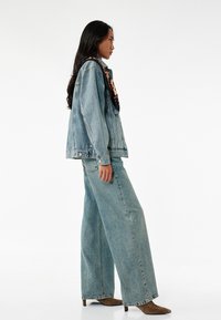 Vaalean sininen farkkutakki, jossa on etutaskut, yhdistettynä leveälahkeisiin, korkeavyötäröisiin vaaleansinihin farkkuihin. Mallilla on päällään teräväkärkiset ruskeat saappaat.