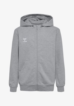 To børn, en pige og en dreng, iført matchende grå hættetrøjer og hvide sneakers, står mod en ensfarvet baggrund.