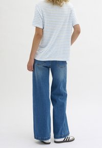 Camiseta de rayas azul claro y blanca, de corte relajado, combinada con jeans de mezclilla azul de pierna ancha. El calzado presenta rayas en blanco y negro.