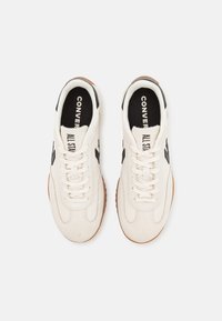 Weiße Leinenschuhe mit schwarzen Akzenten, die eine abgerundete Zehenpartie, Schnürsenkel und eine Gummisohle haben. Auf der Zunge steht der Text "CONVERSE ALL STAR".