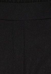 Sort stof med lodret søm og ribstrikket taljebånd, der viser tekstur og syningsdetaljer.