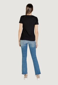 Maglietta nera a maniche corte abbinata a jeans chiari a palazzo, con una leggera sbiaditura. Scarpe da ginnastica bianche completano l'outfit.