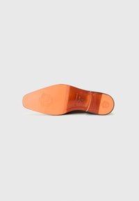 Suela de zapato de cuero en marrón claro con una superficie lisa, que presenta un logo estampado y ranuras para el agarre, moldeada con una ligera curvatura.