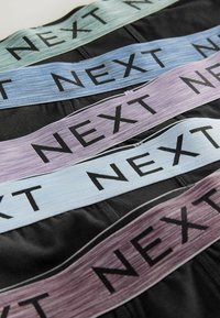 Štiri elastične trakove z besedo "NEXT" v debelih črnih črkah v pastelnih odtenkih zelene, modre in vijolične barve na črni podlagi.