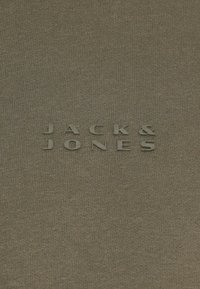 Tkanina w kolorze oliwkowym z wytłoczonym napisem "JACK & JONES" w nieco ciemniejszym odcieniu, o gładkiej, dzianinowej teksturze.