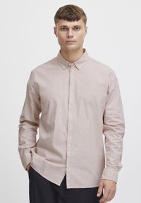 Cămașă cu mâneci lungi și nasturi, având un model cu dungi roz deschis și alb, guler și o tivă curbată. Materialul pare moale și texturat.