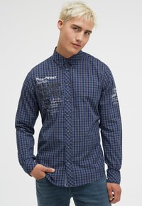 Blau kariertes langärmliges Hemd mit Button-Down-Kragen, ausgestattet mit gesticktem Text und einer Taschenriegelung auf der linken Seite.