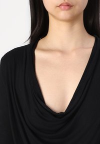 Black draped top with a deep V-neckline, featuring soft fabric and a relaxed fit that gently falls over the collarbone.