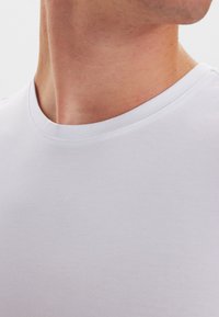 White cotton T-shirt with a crew neckline, featuring a smooth texture and minimal stitching details, highlighting the fabric's softness.
