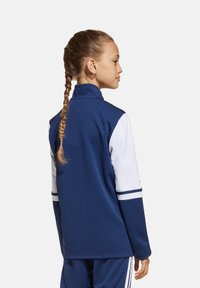 Marineblaues Sportjackett mit Stehkragen, weißen Ärmeln und gestreiften Akzenten. Hergestellt aus glattem, leichtem Stoff.