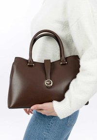 Borsa a mano in pelle marrone con forma strutturata, caratterizzata da un accento in metallo circolare dorato, due manici e una superficie liscia.