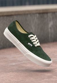 Grüne Wildleder-Sneaker mit weißer Gummisohle und Schnürsenkeln, ausgestattet mit einem kleinen Logotag an der Seite und einem glatten, strukturierten Obermaterial.