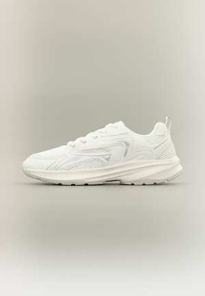Sneaker da atletica bianca con mesh e sovrapposizioni sintetiche, design con lacci e suola spessa e imbottita, mostrata di profilo su uno sfondo neutro.