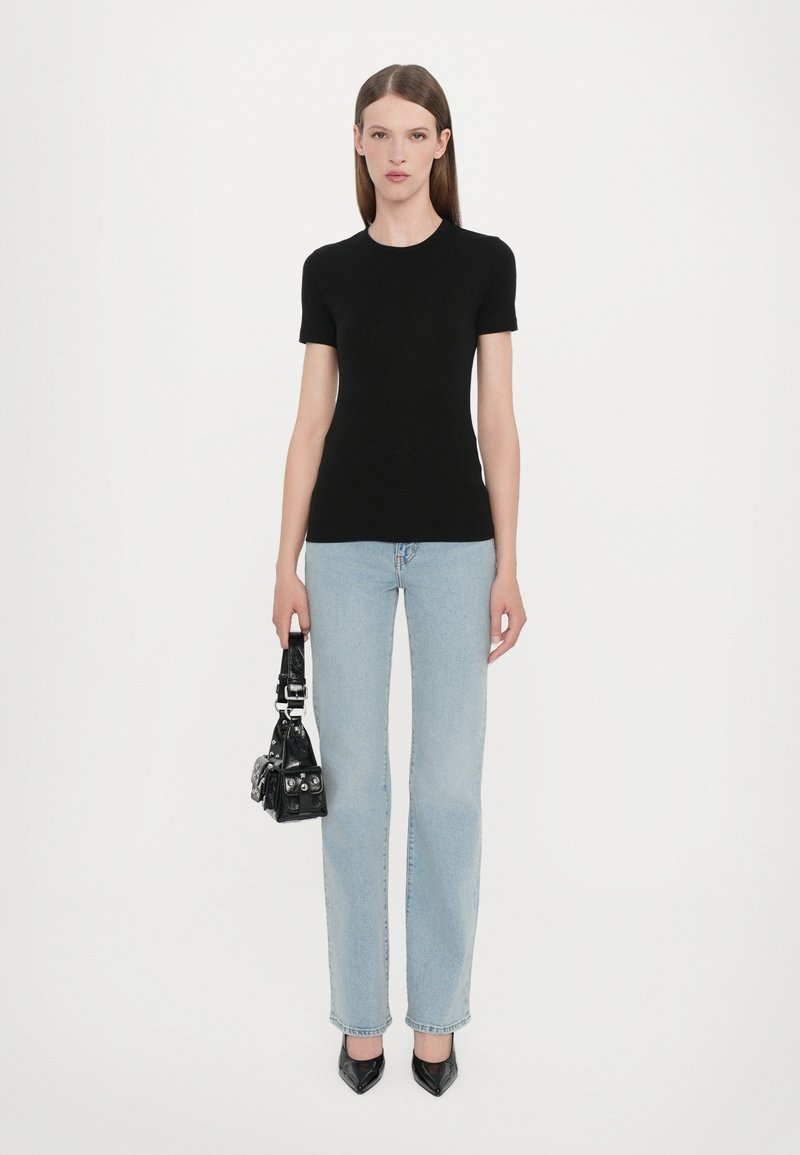 Top aderente nero a maniche corte abbinato a jeans dritti azzurri chiari. La modella tiene una piccola borsa nera con inserti argentati. Tacchi neri a punta.