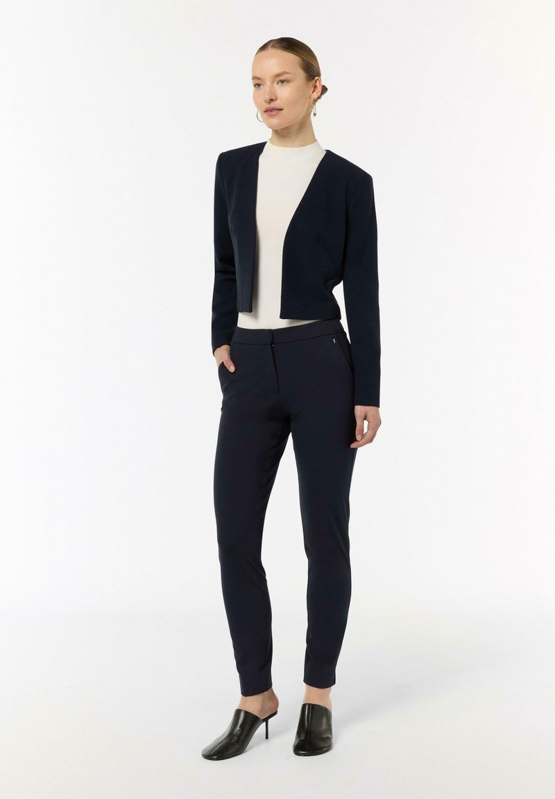 Giacca cropped blu marina, top aderente crema e pantaloni blu marina a sigaretta. Muli neri con tacco completano il look. Design semplice con dettagli minimi.