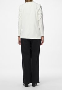 Valkoinen bleiseri, jossa on pitkät hihat ja hyvin istuva leikkaus näkyy takaa, yhdistettynä korkeavyötäröisiin mustiin leveälahkeisiin housuihin.