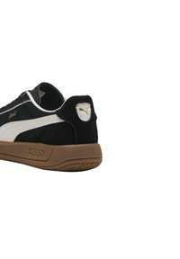 Zapatilla en blanco y negro con parte superior de ante, suela de goma, marca dorada y un parche texturizado en el talón con un detalle de logotipo.