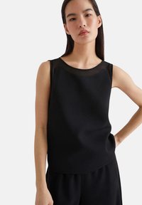 Top nero senza maniche con scollatura rotonda e dettagli in trasparente. Tessuto morbido e vestibilità comoda. Adatto per abbigliamento casual o formale.