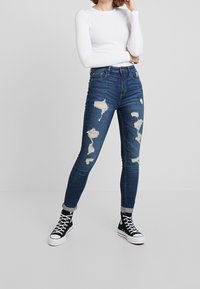 Tunna blå denimjeans med slitna detaljer, med rivna partier på framsidan, sliten look och hög midja. Matchas med svarta sneakers.