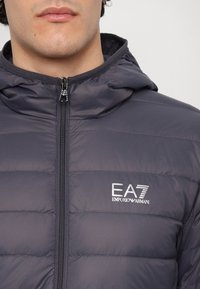Marineblå hettejakke med foret design, frontglidelås og EA7 Emporio Armani-logo på brystet. Glatt, lett stoff.