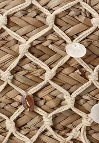 Alfombra de paja tejida que presenta un patrón de diamantes, con cuerdas beige y conchas decorativas intercaladas a lo largo del diseño.