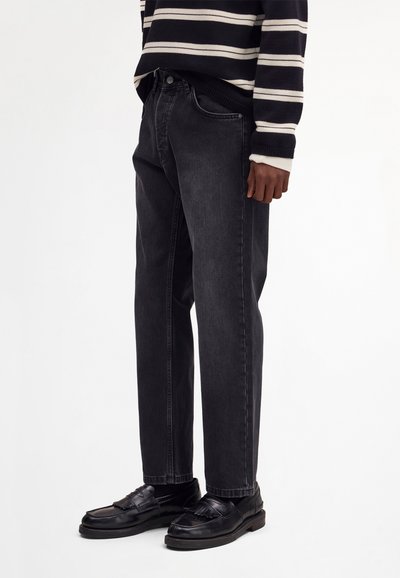 Henkilö, jolla on mustat suorat farkut, mustat nahkaiset loaferit ja mustavalkoraidallinen pitkähihainen neulepaita.