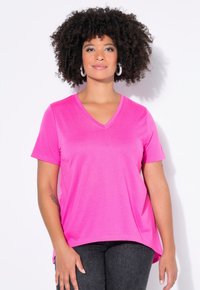 Leuchtend pinkes V-Ausschnitt-T-Shirt, kurze Ärmel, weicher Stoff, lockere Passform, Seitenschlitze. Kombiniert mit dunkelgrauen Jeans.