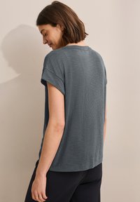 Grey short-sleeve top with a textured fabric, relaxed fit, and rolled cuffs. The back is slightly longer than the front.