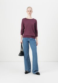 Burgundy stickad tröja med ribbad nederkant, i kombination med ljusblå vida jeans. En svart handväska och svarta platta skor fulländar outfiten.
