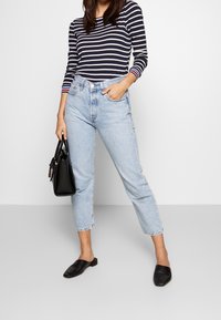 Stribet navy og hvid langærmet top parret med lyseblå højtaljede jeans, sort læderhåndtaske og sorte flade sko med strukturelle detaljer.