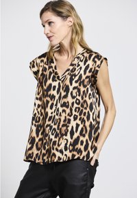 Ärmelloses Oberteil mit Leoprint und V-Ausschnitt, aus glattem Stoff mit einer lockeren Passform, kombiniert mit schwarzen Hosen.
