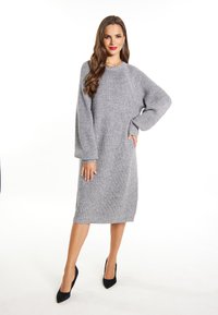 Abito grigio a maglia, di lunghezza media, con vestibilità ampia e maniche lunghe con polsini. Superficie testurizzata, orlo a coste, abbinato a tacchi a punta neri.