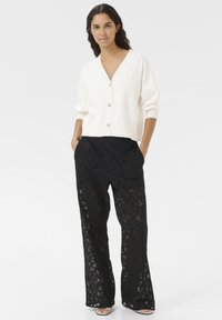 White knitted cardigan with a V-neck and three buttons, paired with black lace wide-leg pants featuring a geometric pattern.