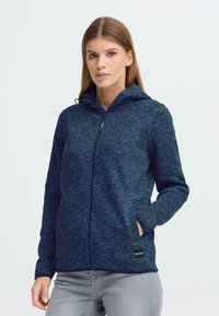 Jūras spēku teksturēts zip-augšējais kapucis ar kapuci, garām piedurknēm, sānu kabatām un logo uz apakšējā mala. Mīksts, ikdienišķs audums.