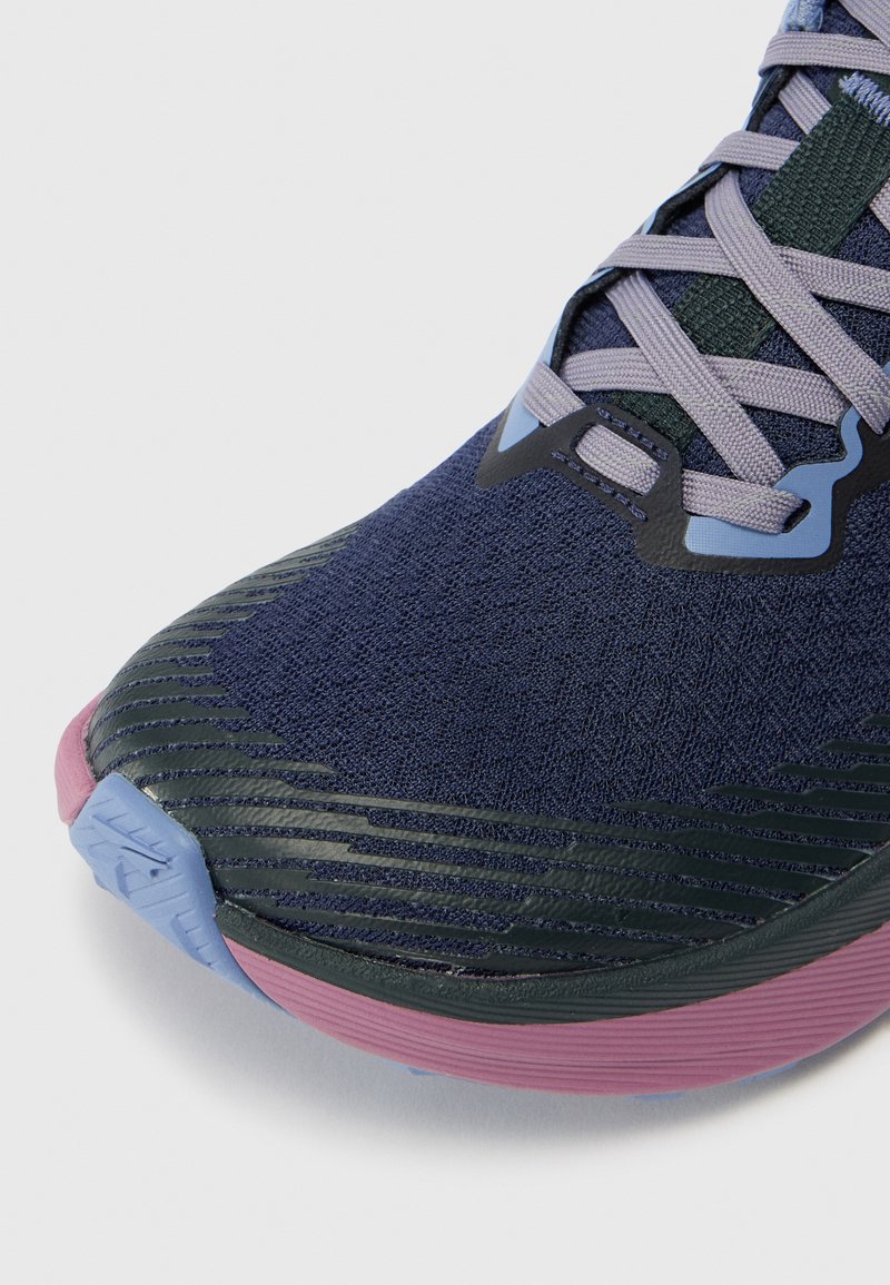 Zapatilla de running en color navy con parte superior de punto texturizado, suela de goma y acentos en rosa y azul. Presenta cordones de color gris claro y superposiciones sintéticas.