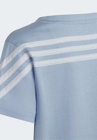 Ljusblå t-shirt med vita vertikala ränder på baksidan, rundad hals, korta ärmar och en mjuk, bomullsliknande textur.