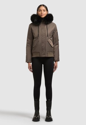 Pruun isoleeritud jakk musta karvaga vooderdatud kapuutsiga, ees taskud ja nöörid, kombineeritud mustade retuuside ja pahkluu saapadega.