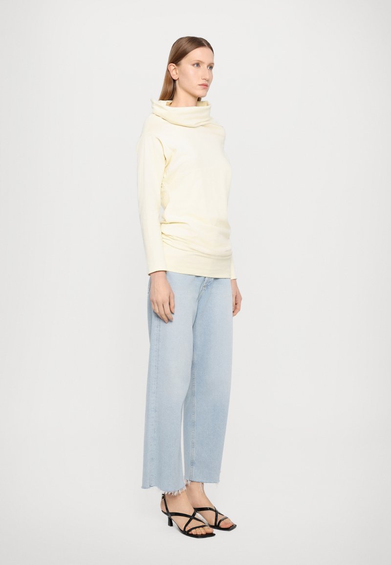 Krämliknande topp med cowl-hals, kombinerad med ljusblå vida jeans och svarta klacksandaler med remmar. Slät tyg och avslappnad passform.
