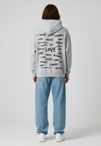 Felpa grigia con varie frasi "amore" stampate in diverse lingue sul retro, abbinata a pantaloni larghi di un blu chiaro.