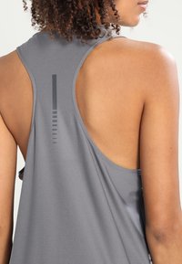 Canotta sportiva grigia con design a schiena di riserbo, texture a coste e dettaglio grafico verticale sul retro. Tessuto leggero.