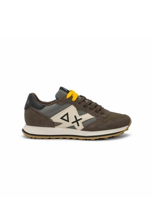Sneaker marrone e grigia con pannello laterale color crema con simboli neri a forma di triangolo e croce, lacci gialli e marroni e suola in gomma.