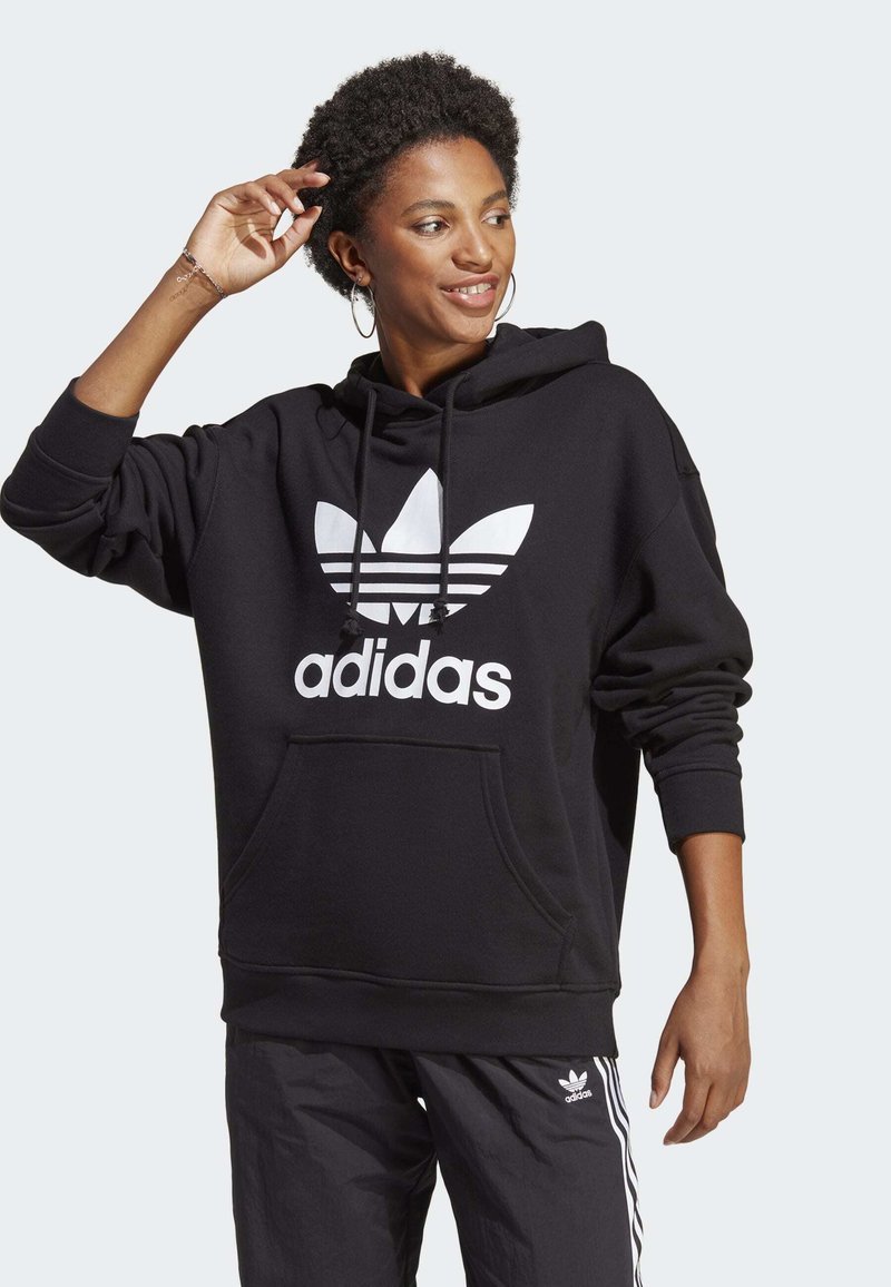 Černá mikina s kapucí a bílým logem Adidas a vzorem tří pruhů. Má přední kapsu a volný střih.